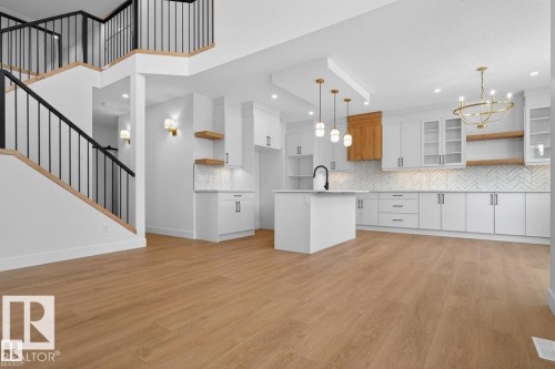 The property features an open-concept layout with light wood flooring, a modern kitchen with white cabinetry and an island, and a staircase with black metal railings - 5 Rosa Crescent, St. Albert, AB - Indoor Photo Showing Kitchen With Upgraded Kitchen