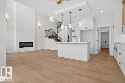 Spacious living area featuring light-toned flooring, a modern fireplace, white walls, and a staircase with black railings - 5 Rosa Crescent, St. Albert, AB - Indoor Photo Showing Kitchen