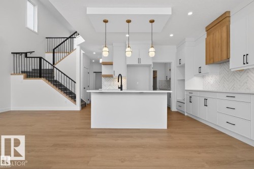 This open-concept area features light wood flooring, a modern kitchen with white cabinetry, a central island, and three pendant lights - 5 Rosa Crescent, St. Albert, AB - Indoor Photo Showing Kitchen With Upgraded Kitchen