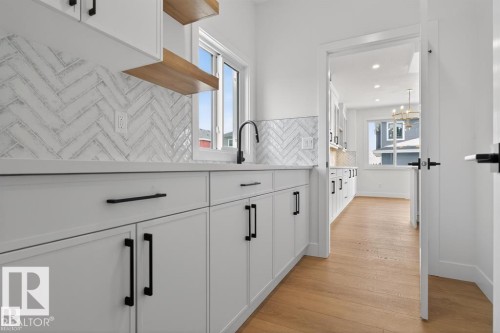 This well-appointed kitchen features white cabinetry with black hardware, open wooden shelving, a white herringbone tile backsplash, and light wood flooring - 5 Rosa Crescent, St. Albert, AB - Indoor Photo Showing Other Room