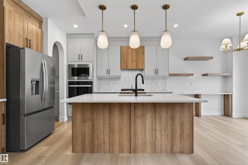 Well-appointed kitchen featuring a large island with a white countertop, modern pendant lighting, and stainless steel appliances - 11 Redbud Way, St. Albert, AB - Indoor Photo Showing Kitchen With Upgraded Kitchen