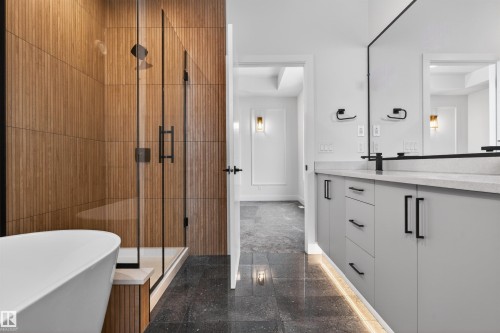 Contemporary bathroom featuring a freestanding tub, a glass-enclosed shower with wood-paneled walls, a double vanity with a light-colored countertop, and dark-toned floor tiles - 11 Redbud Way, St. Albert, AB - Indoor Photo Showing Bathroom