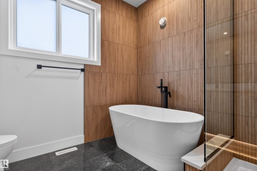 Bathroom featuring a freestanding white bathtub, a black matte floor-mounted tub filler, and wood-paneled walls - 11 Redbud Way, St. Albert, AB - Indoor Photo Showing Bathroom