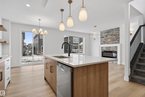 The open-concept living space features hardwood floors, a kitchen island with a sink and dishwasher, and a living area with a stone-clad fireplace - 11 Redbud Way, St. Albert, AB - Indoor Photo Showing Kitchen With Upgraded Kitchen