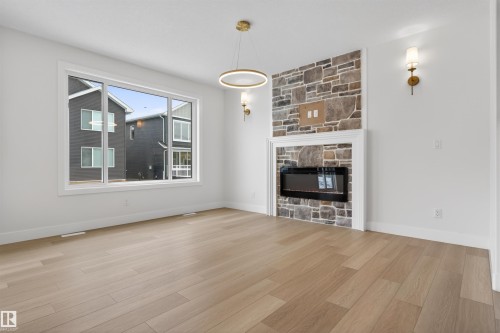 This inviting room features light-toned wood flooring, an electric fireplace with a stone surround, and a large window providing natural light - 11 Redbud Way, St. Albert, AB - Indoor Photo Showing Living Room With Fireplace