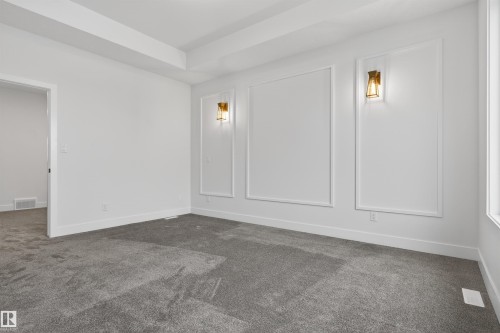 Spacious room featuring tray ceilings, decorative wall molding, and modern sconce lighting - 11 Redbud Way, St. Albert, AB - Indoor Photo Showing Other Room