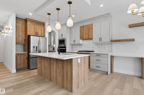 The kitchen features a central island with a white countertop, light wood cabinetry, and stainless steel appliances - 11 Redbud Way, St. Albert, AB - Indoor Photo Showing Kitchen With Upgraded Kitchen