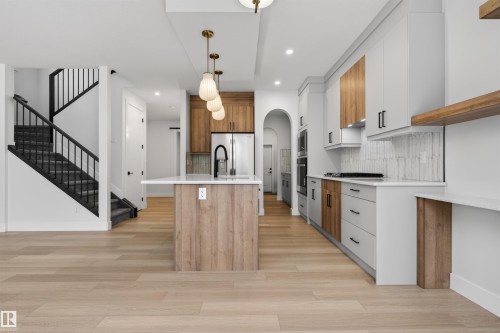 The kitchen features a central island with a waterfall countertop, pendant lighting, and a stainless steel refrigerator - 11 Redbud Way, St. Albert, AB - Indoor Photo Showing Kitchen With Upgraded Kitchen