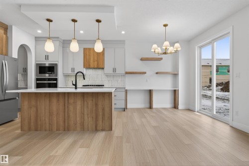 This kitchen features a central island with a wood-look base, a white countertop, and three pendant lights overhead - 11 Redbud Way, St. Albert, AB - Indoor Photo Showing Kitchen With Upgraded Kitchen