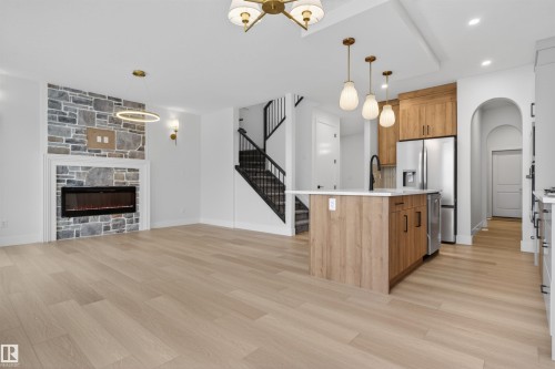 This open-concept living space features light-toned wood flooring, a stone-faced fireplace, and a kitchen island with pendant lighting - 11 Redbud Way, St. Albert, AB - Indoor Photo Showing Kitchen With Fireplace With Upgraded Kitchen