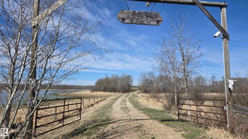 Entry gate with a wooden overhead sign, a gravel drive, and a body of water - 11 Twin Lakes Drive, Rural Lamont County, AB 