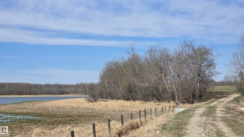 Expansive undeveloped land featuring a dirt track, a wire fence, mature trees, a natural body of water, and broad open space - 11 Twin Lakes Drive, Rural Lamont County, AB 