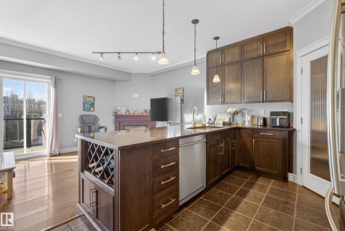 The kitchen features dark wood cabinetry, a central island with a built-in wine rack, and a dishwasher - 307 9750 94 Street, Edmonton, AB - Indoor Photo Showing Kitchen