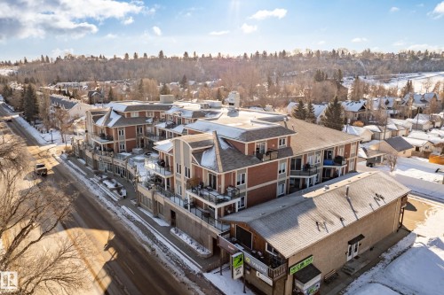 This property features a multi-story building with brick accents and balconies, situated along a road with a treed hill in the background - 307 9750 94 Street, Edmonton, AB - Outdoor With View