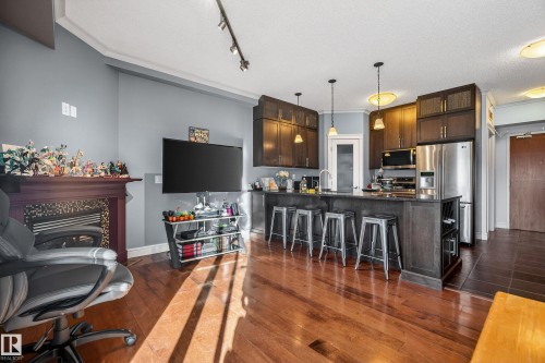 Open-concept living space featuring hardwood flooring, a fireplace, and a kitchen island with seating - 307 9750 94 Street, Edmonton, AB - Indoor Photo Showing Kitchen With Upgraded Kitchen