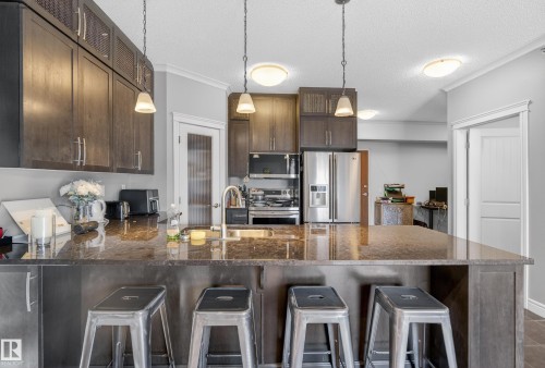 The kitchen features dark wood cabinetry, stainless steel appliances, a large island with a stone countertop, and pendant lighting - 307 9750 94 Street, Edmonton, AB - Indoor Photo Showing Kitchen With Upgraded Kitchen