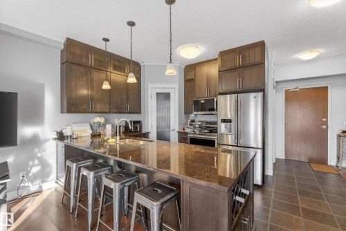 The kitchen features dark wood cabinetry, stainless steel appliances, and a large central island with a granite countertop and integrated wine rack - 307 9750 94 Street, Edmonton, AB - Indoor Photo Showing Kitchen With Upgraded Kitchen