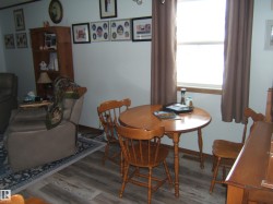 This inviting living area features wood-look flooring, a window with brown curtains, and a wooden dining table with chairs - 