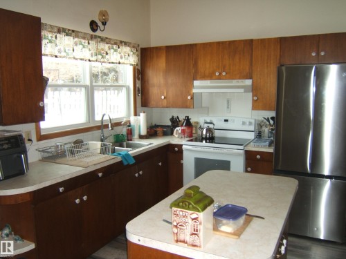 The kitchen features wood cabinetry, a white tile backsplash, and a stainless steel refrigerator - 4702 52 Avenue, Two Hills, AB - Indoor Photo Showing Kitchen