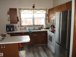 The kitchen features wood cabinetry, a stainless steel refrigerator, and a white oven with a matching range hood - 