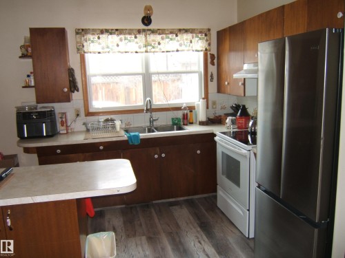 The kitchen features wood cabinetry, a double basin sink, and a window above the sink - 4702 52 Avenue, Two Hills, AB - Indoor Photo Showing Kitchen With Double Sink