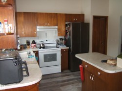 The kitchen features wood cabinetry, a stainless steel refrigerator, white range, and a kitchen island with a light-colored countertop - 