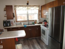 The kitchen features wood cabinetry, a double basin sink, and a window above the sink - 