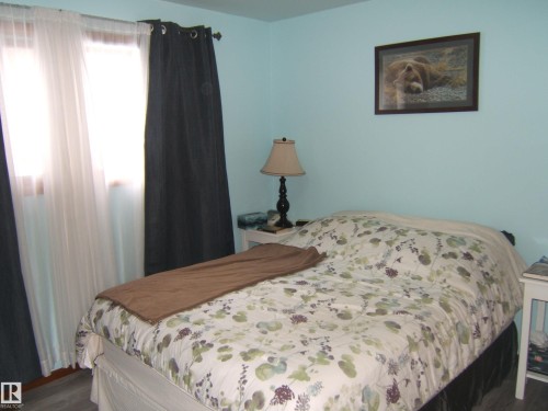 The room features light blue walls and a window with sheer white and dark curtains - 4702 52 Avenue, Two Hills, AB - Indoor Photo Showing Bedroom