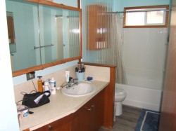 Bathroom featuring a single vanity with a white sink, a mirror with wood framing, and a white bathtub with an overhead shower and a window - 