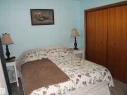 This bedroom features light blue walls, a bed with a floral comforter, and wood-paneled closet doors - 