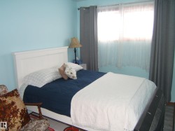 This room features light blue walls, a window with sheer and opaque curtains, and a nightstand with a lamp - 