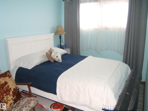 This bedroom features light blue walls, a window with sheer and blackout curtains, and wood flooring - 4702 52 Avenue, Two Hills, AB - Indoor Photo Showing Bedroom