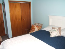 The room features light blue walls, a white headboard, and a wooden closet with bi-fold doors - 