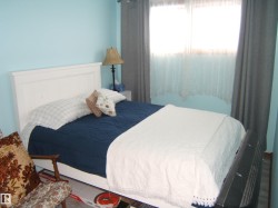 This bedroom features light blue walls, a window with sheer and blackout curtains, and wood flooring - 