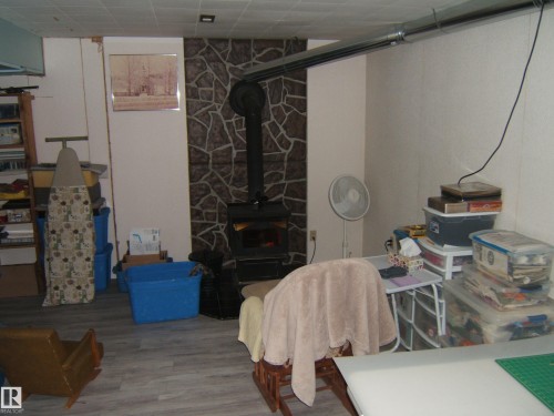 This room features a wood-burning stove with a stone-clad surround and wood-effect flooring - 4702 52 Avenue, Two Hills, AB - Indoor Photo Showing Other Room