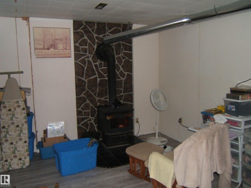 The room features a wood-burning stove with a stone-accented wall and a grey floor - 4702 52 Avenue, Two Hills, AB - Indoor