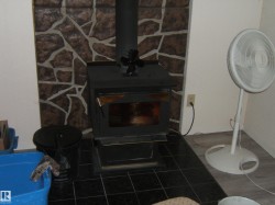 A wood-burning stove with a black stove pipe is situated on a black tiled floor - 