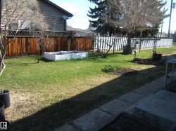 Expansive backyard featuring a manicured lawn, a raised garden bed, mature deciduous trees, and concrete paver steps - 
