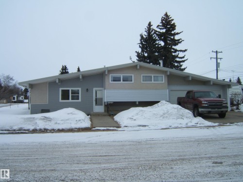 Exterior view of the property featuring a light-colored facade, a front door, and an attached garage - 4702 52 Avenue, Two Hills, AB - Outdoor With Facade