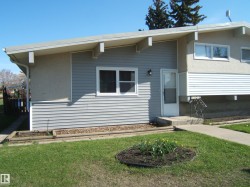 Split-level exterior featuring light gray horizontal siding, stucco elements, white window trim, and a concrete front walkway - 