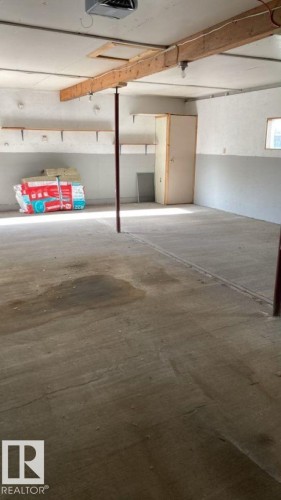 Spacious utility room with concrete flooring, exposed ceiling beams, and shelving for storage - 4702 52 Avenue, Two Hills, AB - Indoor