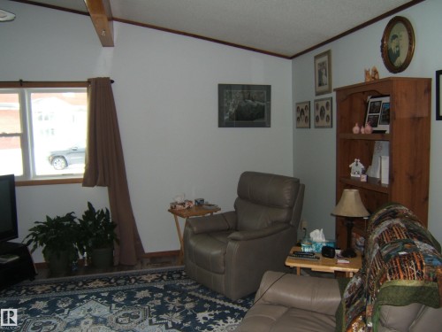 Living space featuring a vaulted ceiling with exposed beam, window with wood trim, and a patterned area rug - 4702 52 Avenue, Two Hills, AB - Indoor