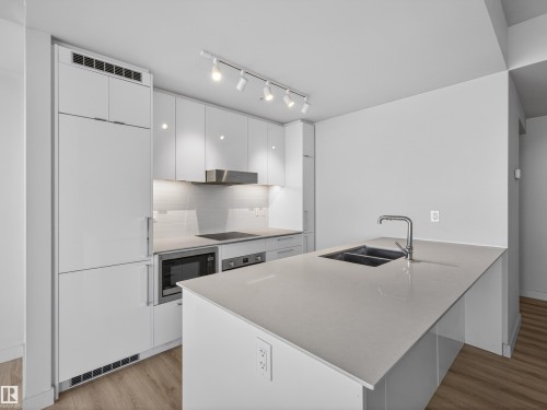 The kitchen features a modern aesthetic with white cabinetry, integrated appliances, and a kitchen island with a double sink and a gooseneck faucet - 2612 10360 102 Street, Edmonton, AB - Indoor Photo Showing Kitchen With Double Sink With Upgraded Kitchen