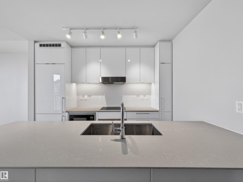 Modern kitchen featuring white cabinetry, a built-in refrigerator, sleek stainless steel appliances, and a large island with an integrated sink - 2612 10360 102 Street, Edmonton, AB - Indoor Photo Showing Kitchen With Upgraded Kitchen