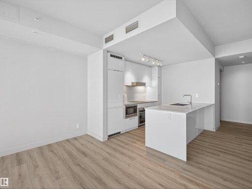 The kitchen features light wood flooring, white cabinetry, a built-in microwave, and an island with an integrated sink and faucet. - 2612 10360 102 Street, Edmonton, AB - Indoor Photo Showing Kitchen