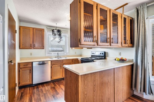 The kitchen features wood cabinetry, a stainless steel dishwasher, a black range, and light-colored countertops - 18923 86A Avenue, Edmonton, AB - Indoor Photo Showing Kitchen With Double Sink