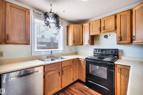 The kitchen features wooden cabinetry, a stainless steel double basin sink, a black electric range, and a stainless steel dishwasher - 18923 86A Avenue, Edmonton, AB - Indoor Photo Showing Kitchen With Double Sink