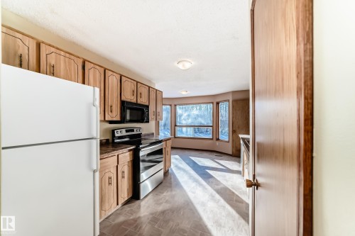 The kitchen features light wood cabinetry, a white refrigerator, a black microwave, and a stainless steel oven and range - 100 23016 Twp Rd 504, Rural Leduc County, AB - Indoor Photo Showing Kitchen