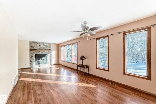 Living space featuring hardwood flooring, a stone fireplace, and windows providing natural light - 100 23016 Twp Rd 504, Rural Leduc County, AB - Indoor With Fireplace
