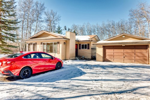 The property features a detached garage with a brown door, a beige exterior, and a snow-covered driveway - 100 23016 Twp Rd 504, Rural Leduc County, AB - Outdoor